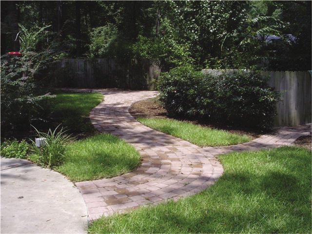 A curved walkway through a grassy lawn. The path forks off toward a wooden fence.